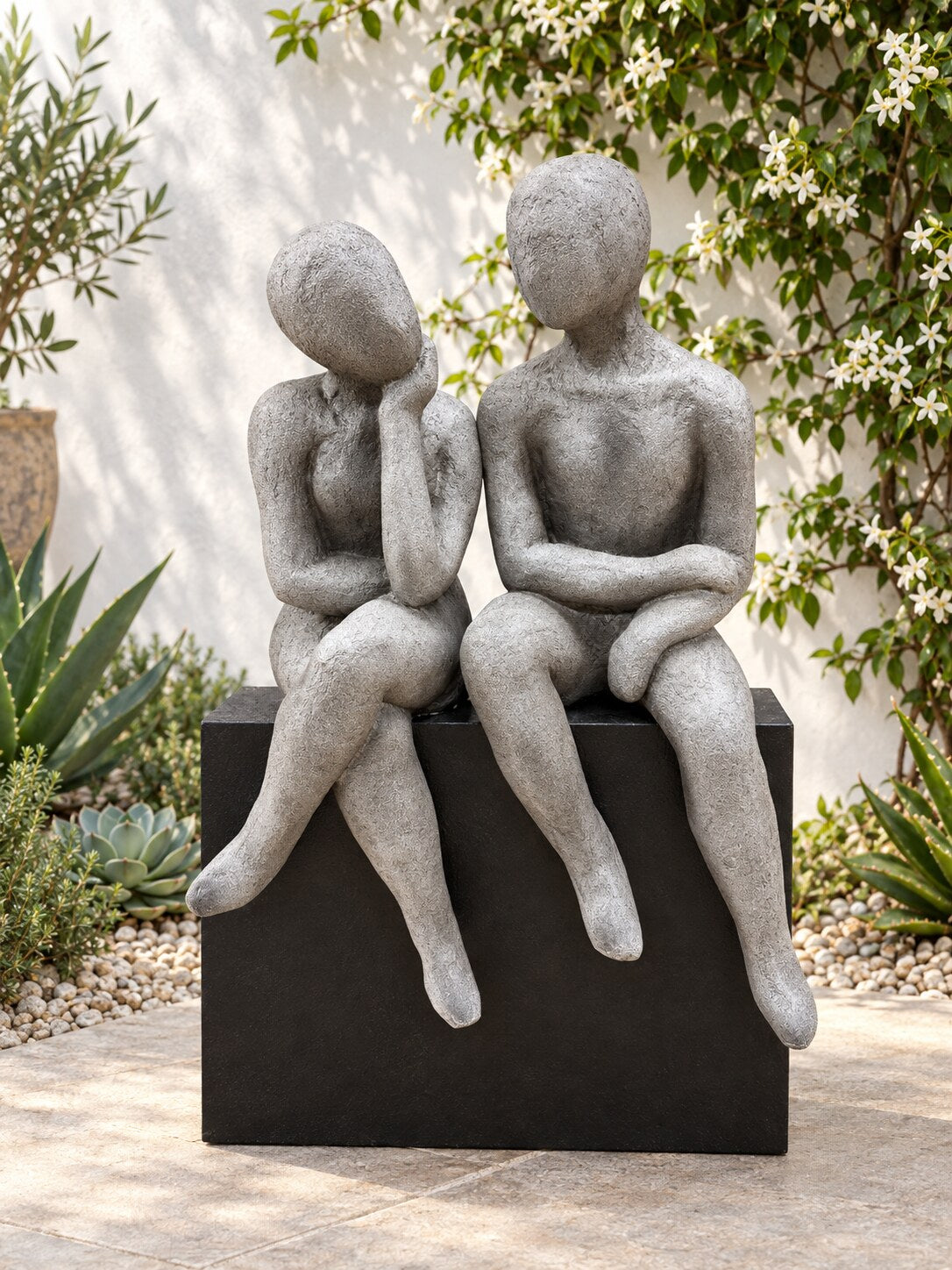 Gustaria abstract talking couple statue on a black plinth in a white courtyard with jasmine