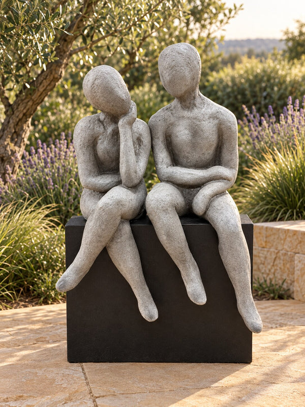 Gustaria sculpture of two grey stylised talking figures sitting on a black base on a garden terrace