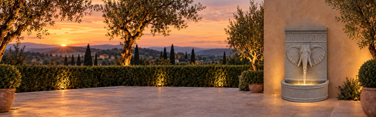 Annibale grey elephant head wall fountain on a Mediterranean terrace at sunset