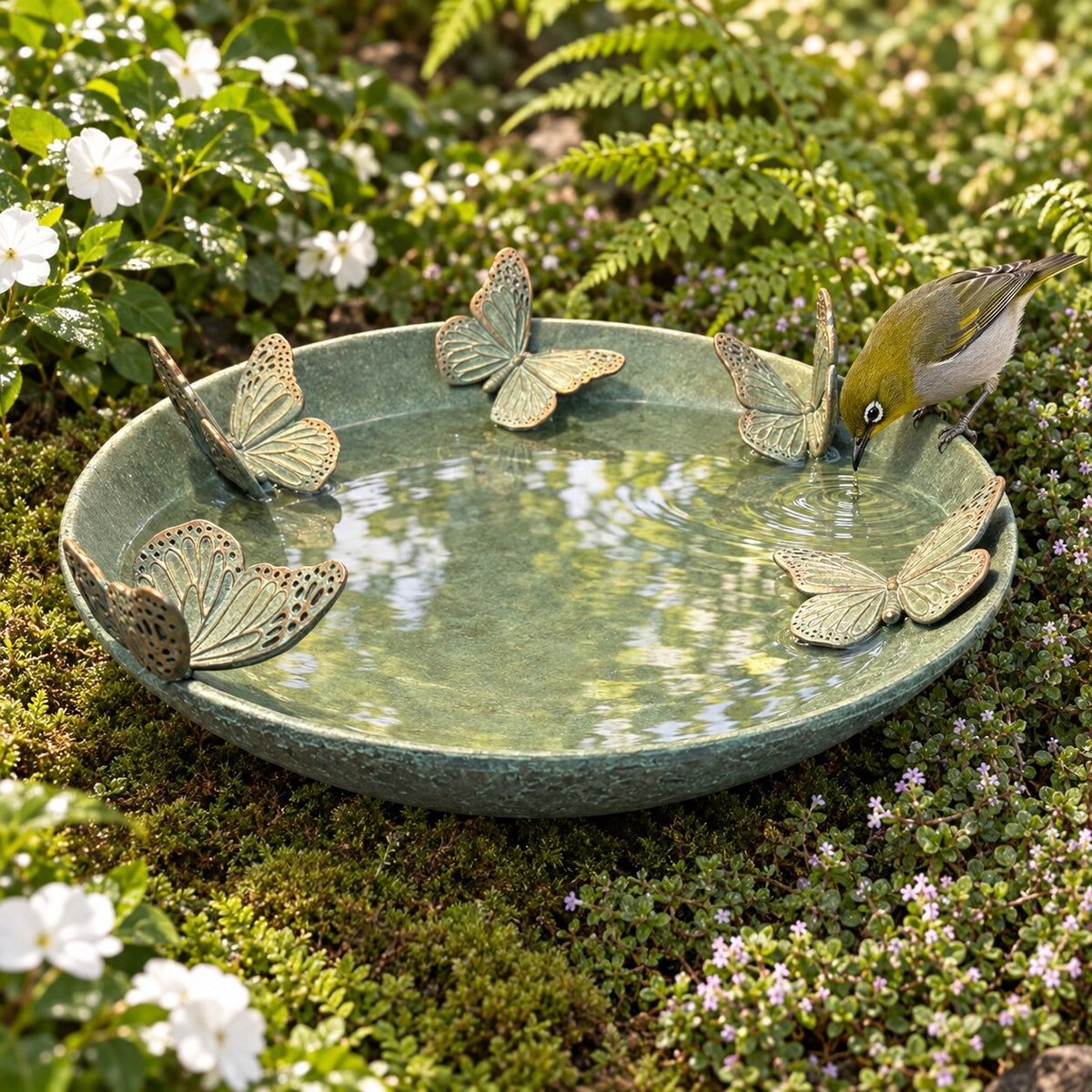 Mariposas verdigris resin bird bath with butterflies in a garden bed with a silvereye bird drinking